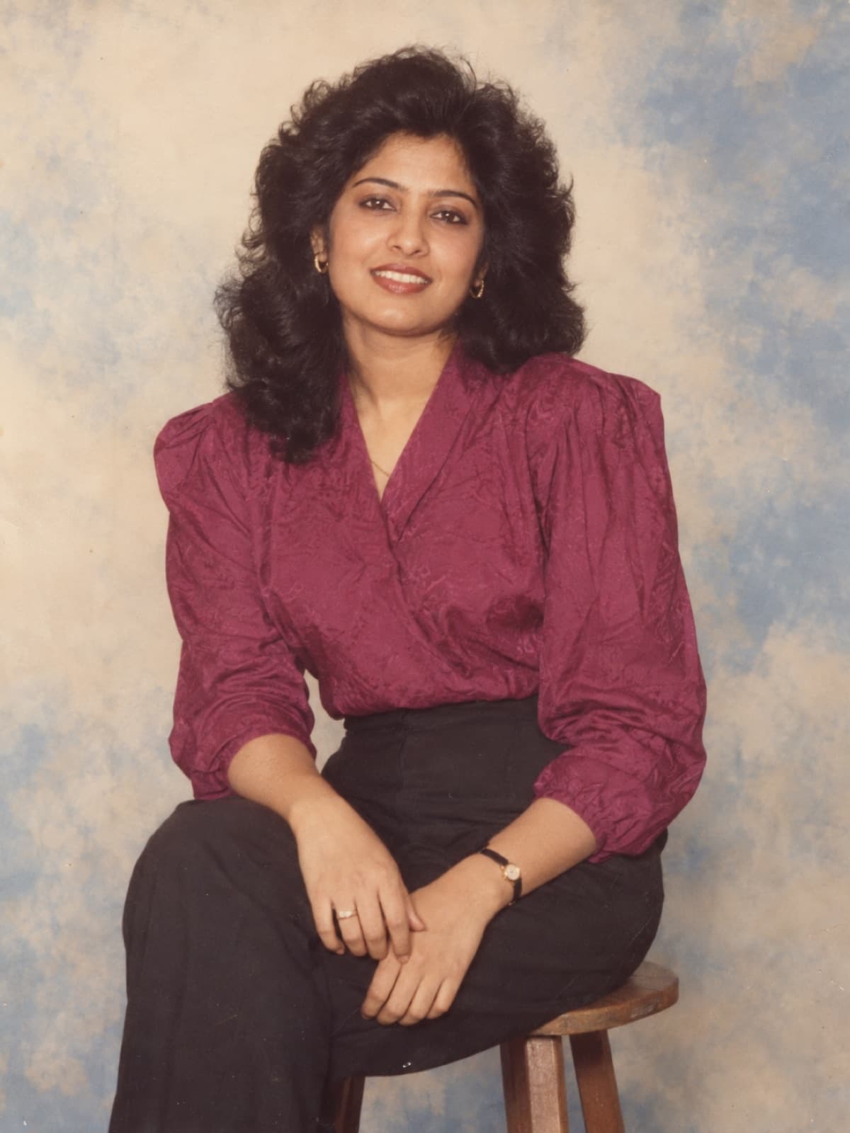 AI-generated example of a South Asian woman in a mid-1980s portrait studio with voluminous hair, a jewel-tone blouse and faded film color