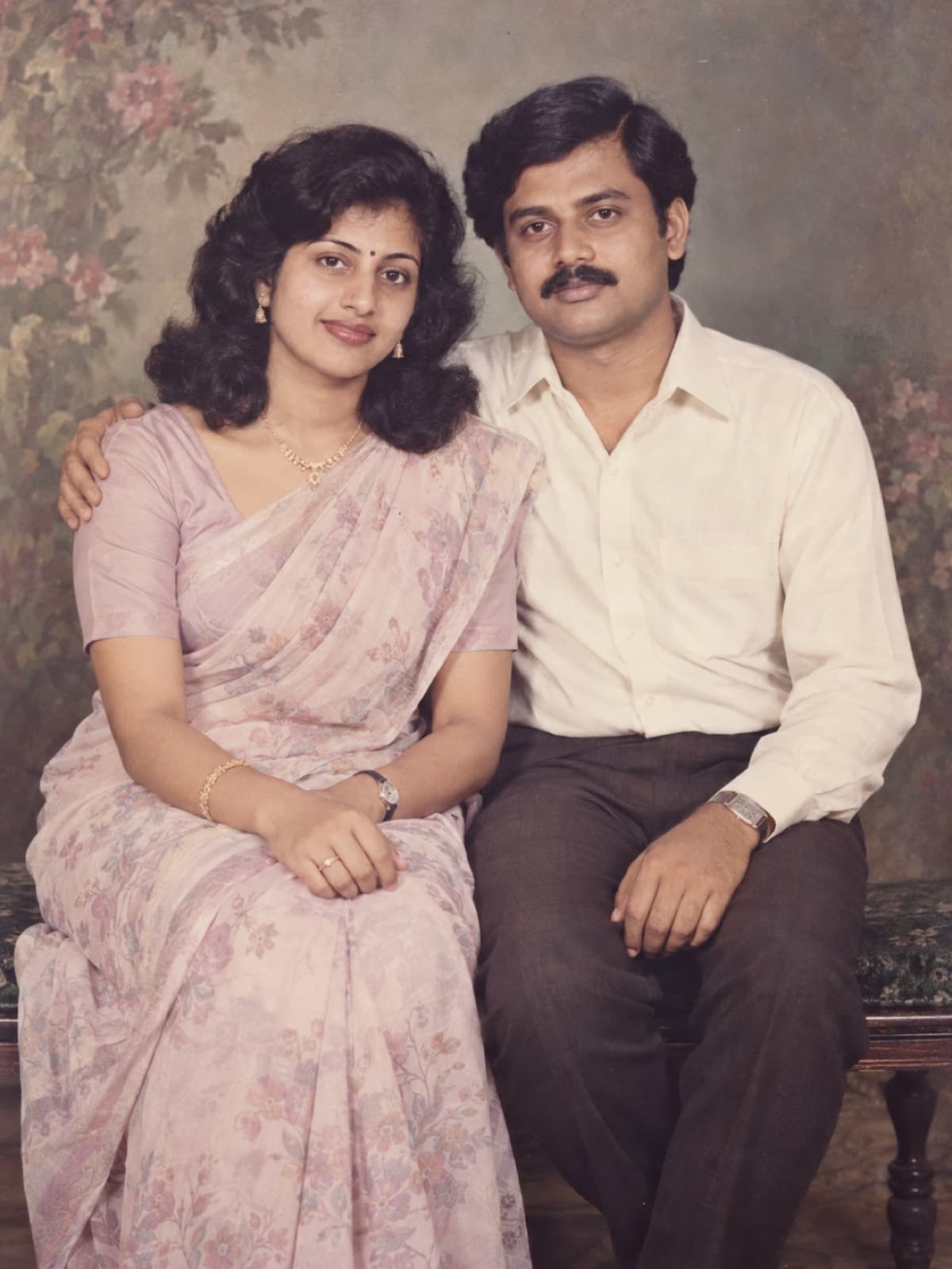 AI-generated example of a South Asian couple posing together in a late-1980s photo studio with a faded floral backdrop