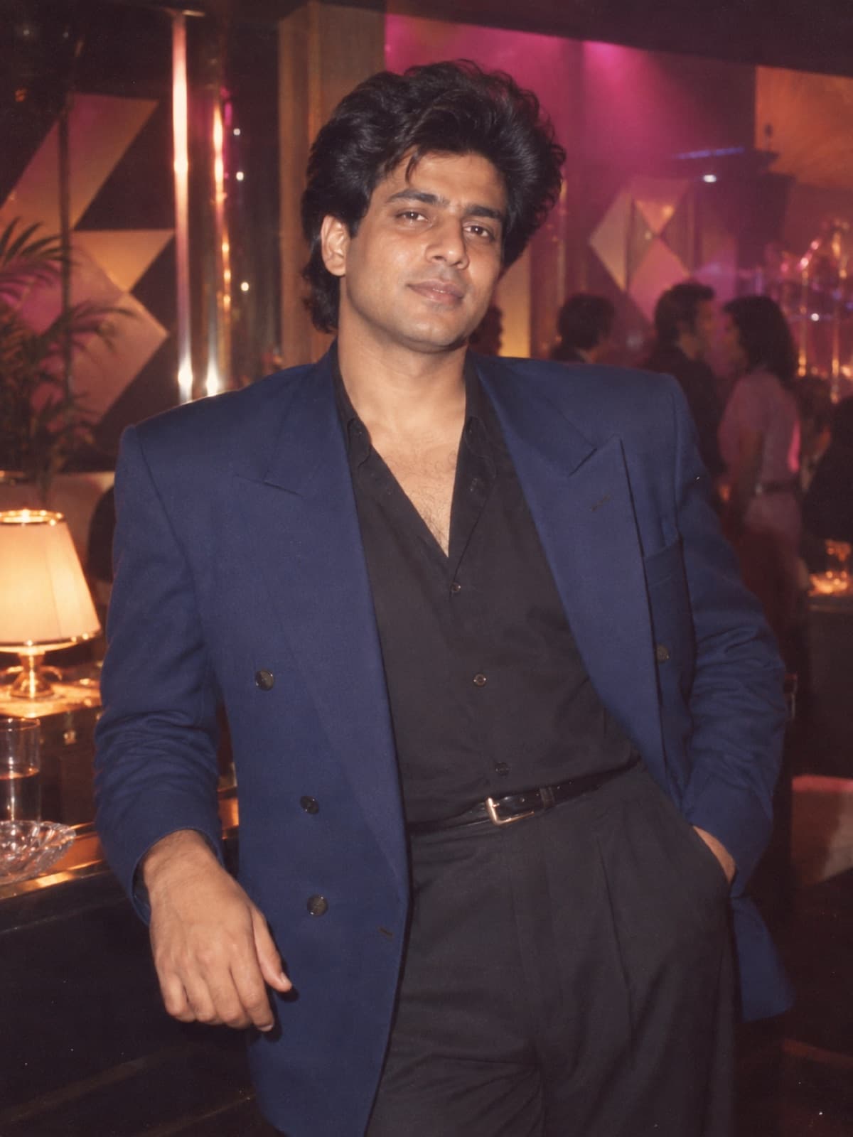 AI-generated example of a South Asian man in a blue late-1980s blazer photographed with direct flash in a nightlife lounge